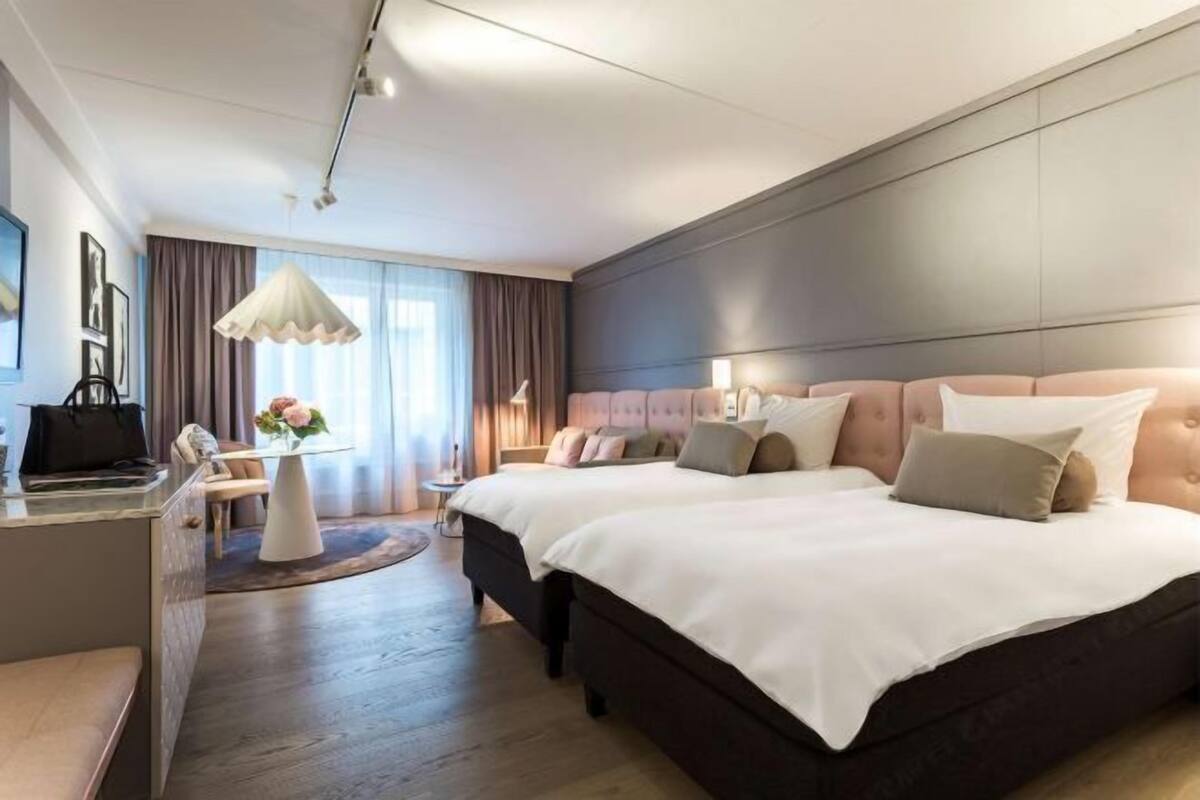 A hotel room with a large bed, a desk, a chair, and a small table with a vase of flowers.