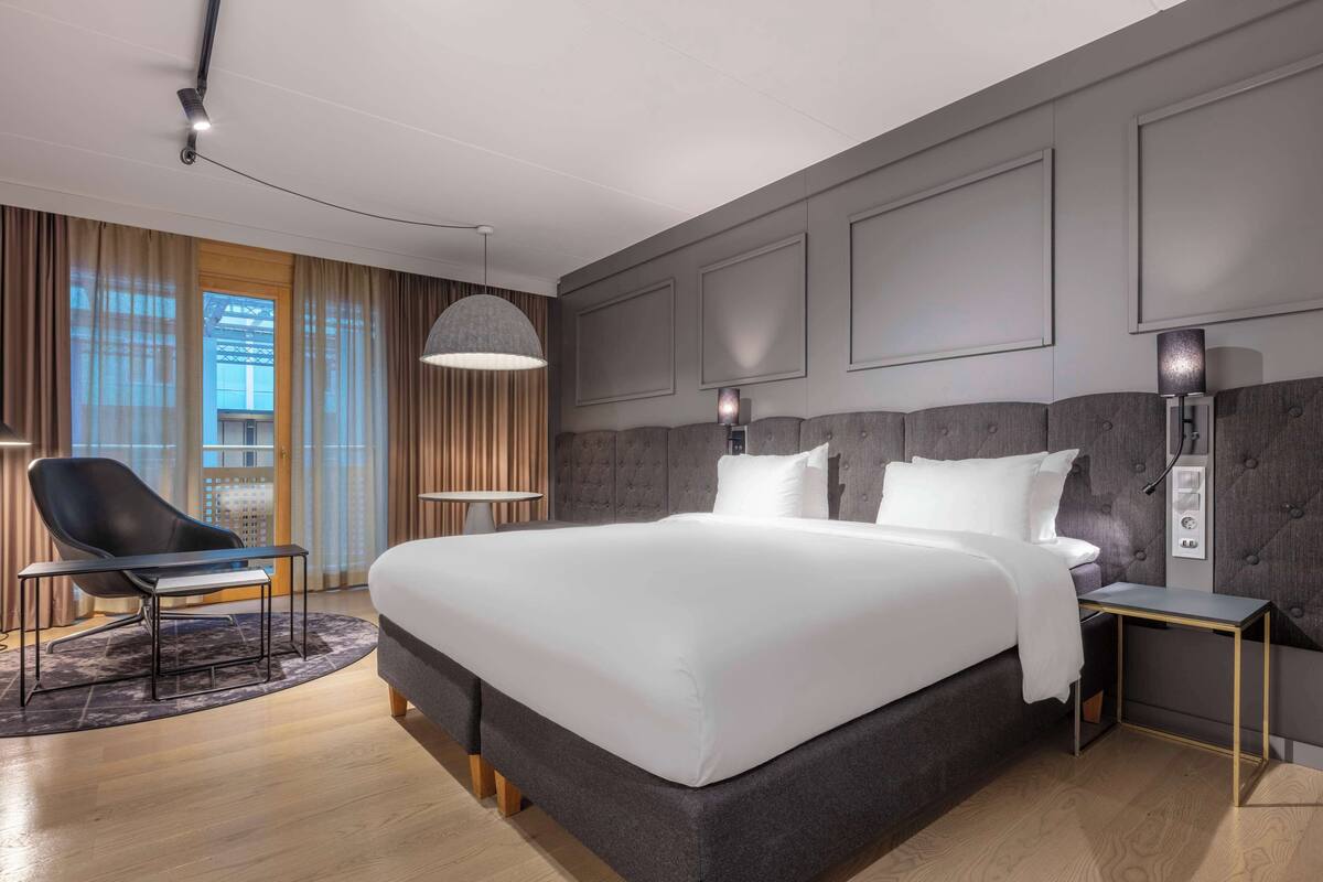 A modern hotel room with a large bed, a desk, and a chair.