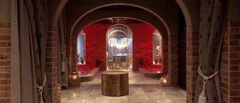 An arched room with brick walls, a central wooden table, and two windows with decorative glass.