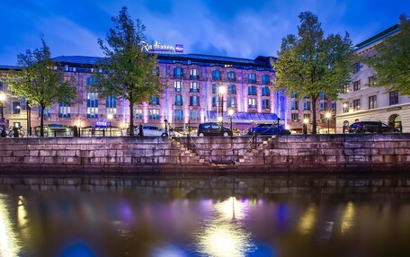 A hotel with a stone facade, multiple windows, and a reflection in the water.