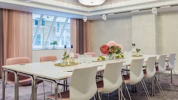 Een vergaderzaal met een lange tafel, zes stoelen, een kroonluchter en een raam met gordijnen.