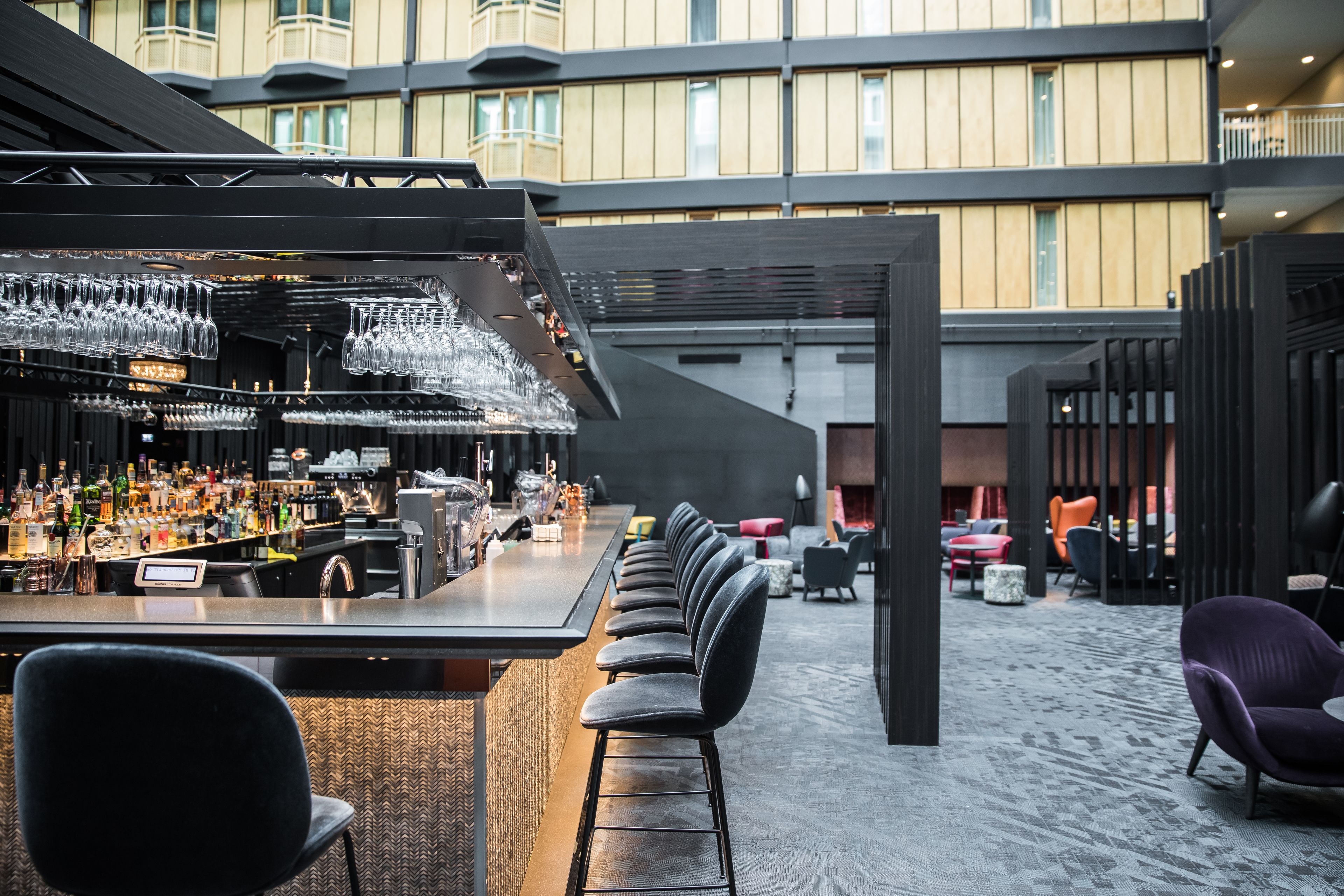 A bar area with a long counter, multiple stools, and a variety of bottles and glasses.
