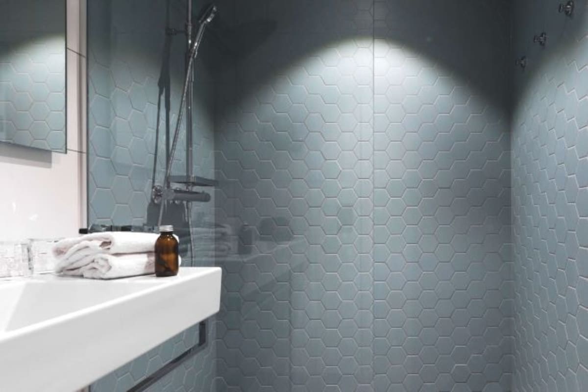 Un baño con lavamanos blanco, espejo y ducha con un diseño de baldosas hexagonales.
