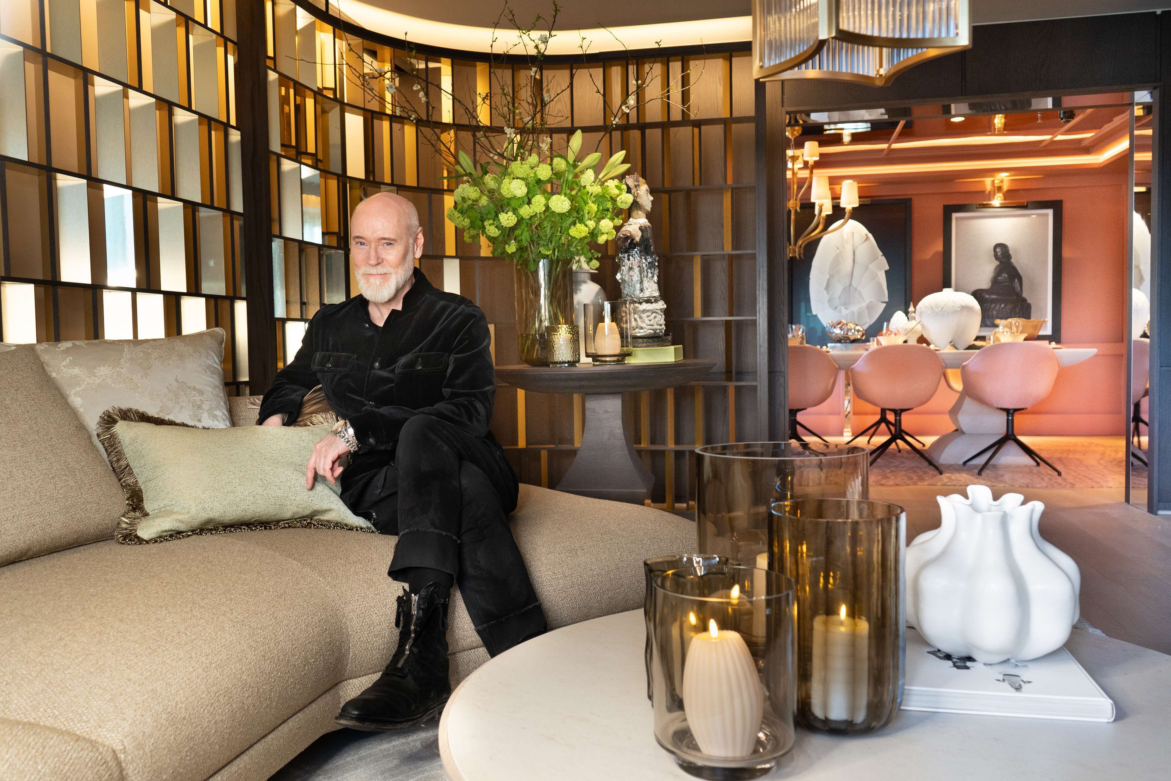 Ein Mann sitzt auf einem Sofa in einem modernen Interieur mit einer dekorativen Vase, Kerzen und einem kleinen Tisch.