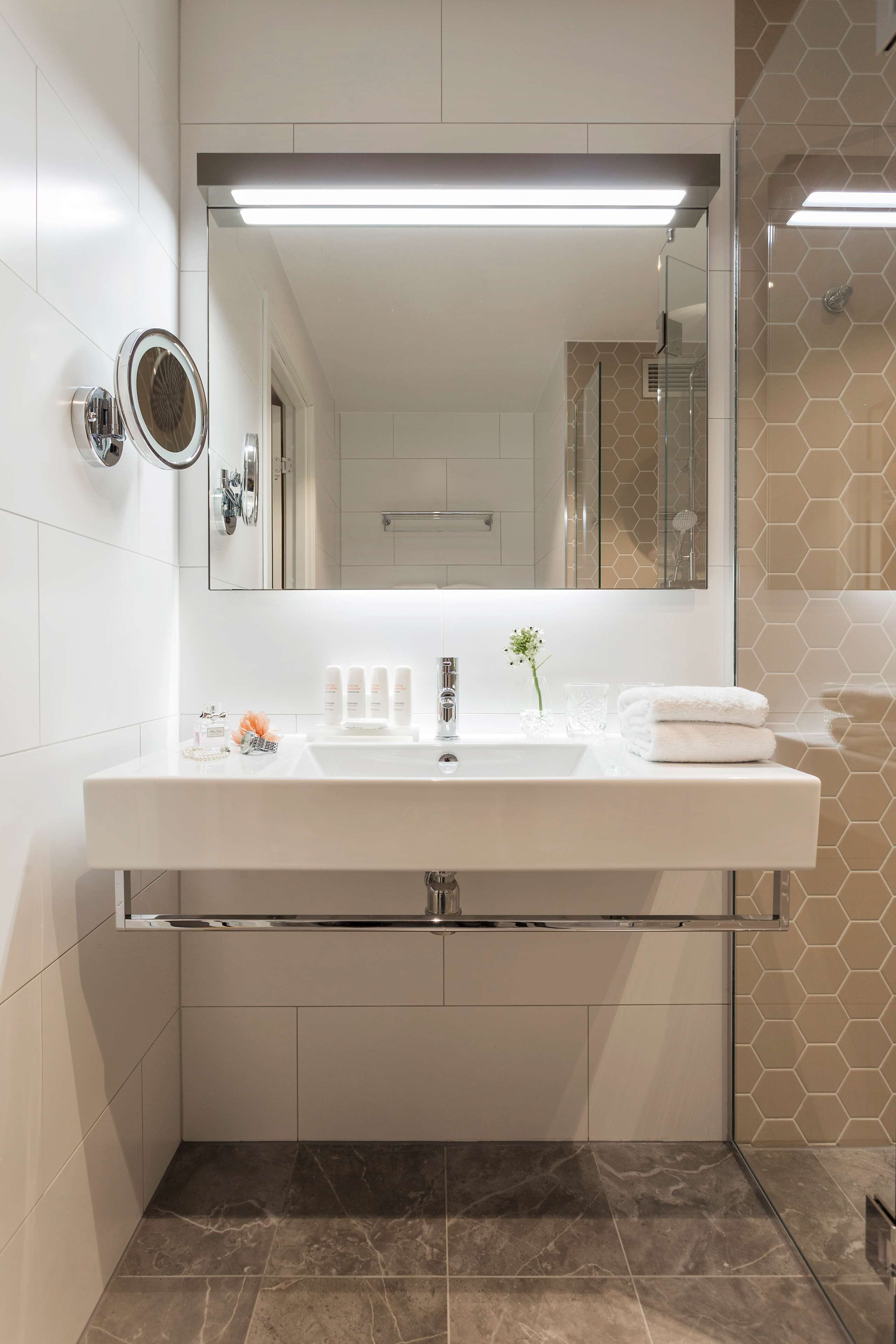 A modern bathroom with a large mirror, white sink, and a glass shower enclosure.