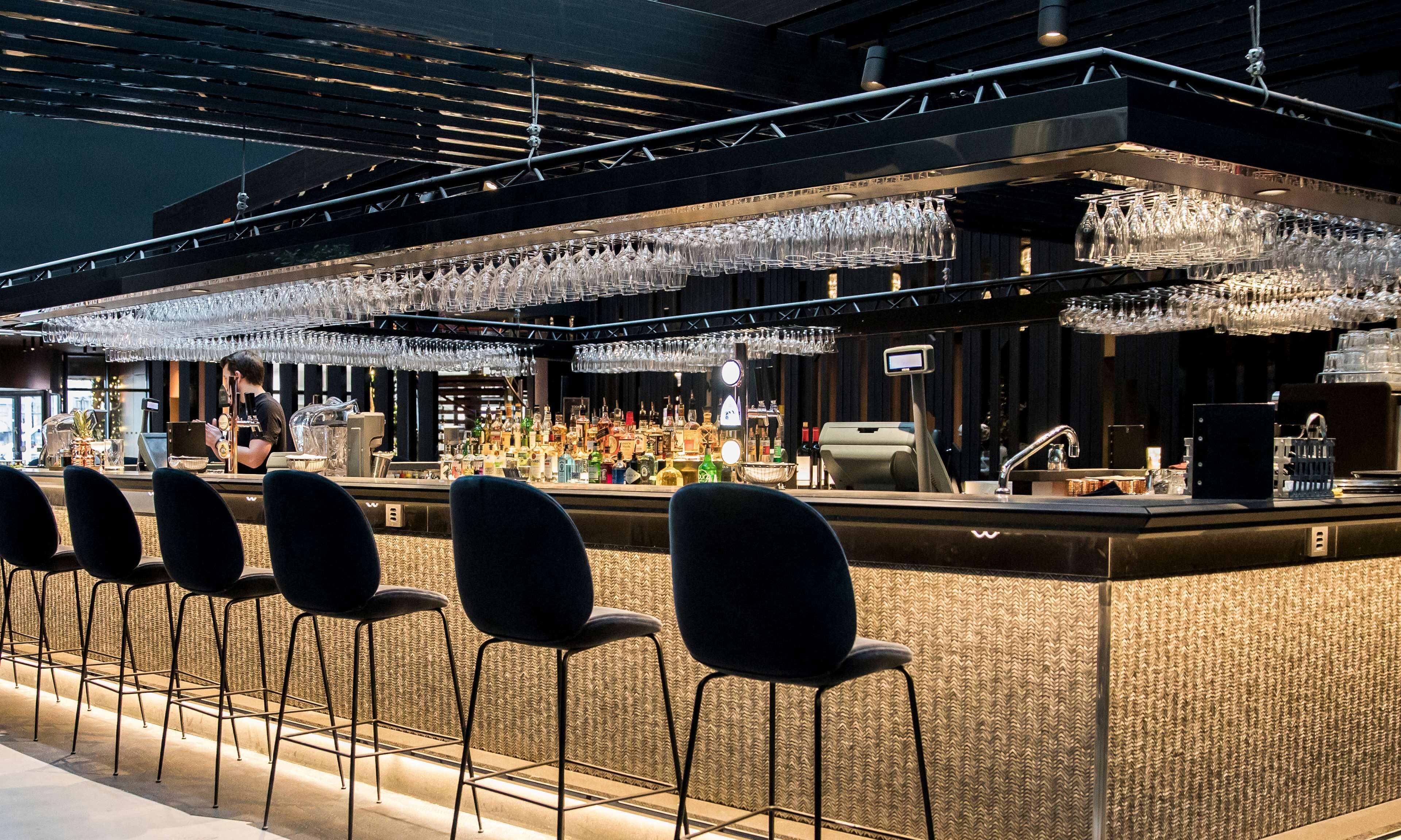 A bar area with a counter, bar stools, and a variety of bottles and glasses.