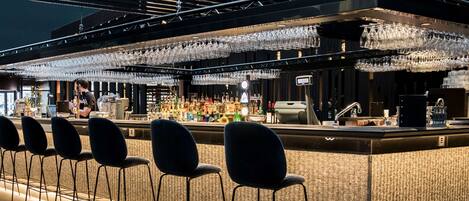 A bar area with a counter, bar stools, and a variety of bottles and glasses.