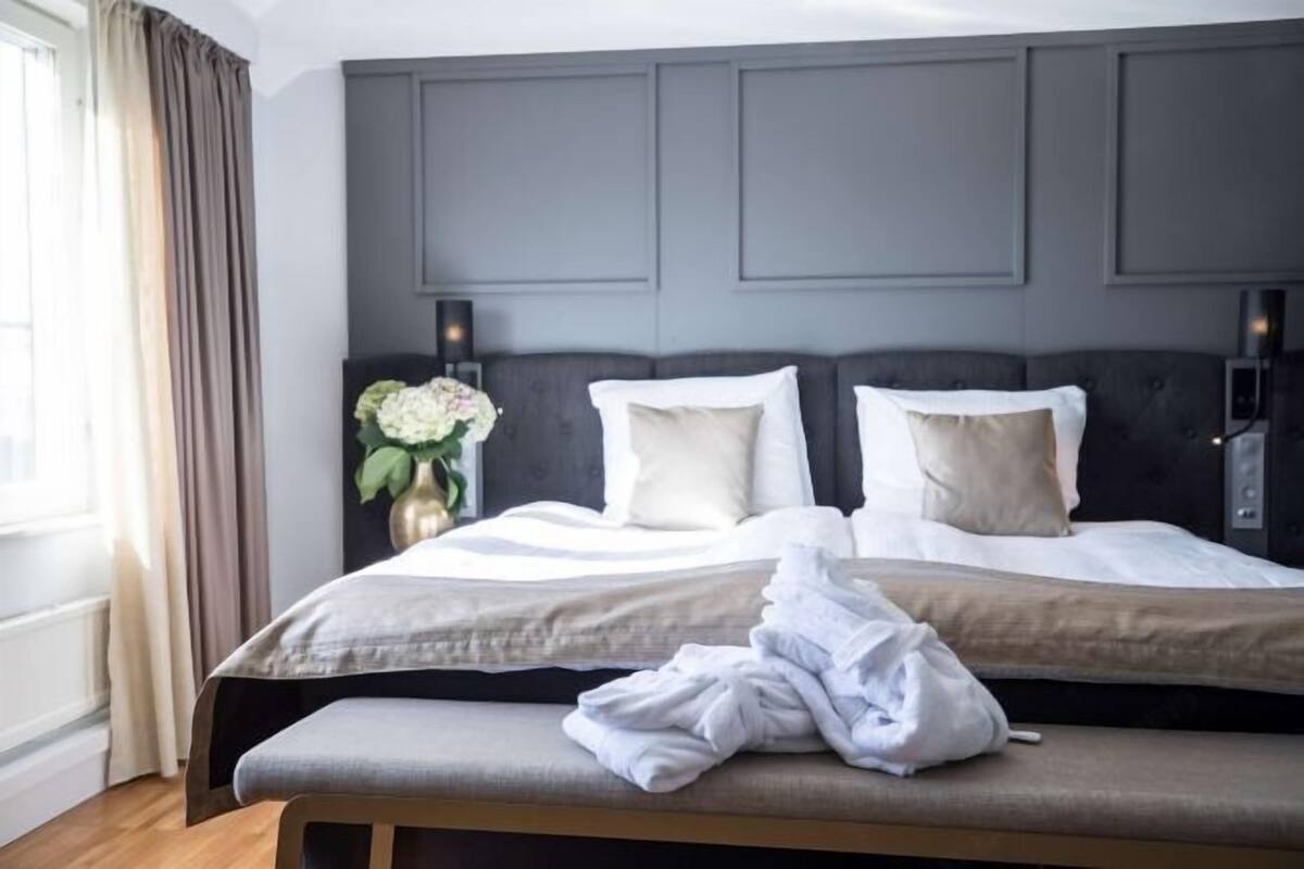A hotel room with a large bed, a bench, and a wall-mounted light fixture.