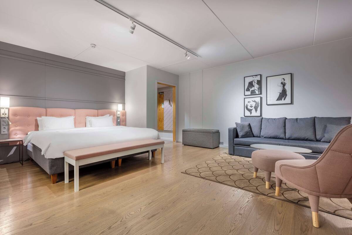 A modern bedroom with a large bed, a bench, a sofa, and a small table.