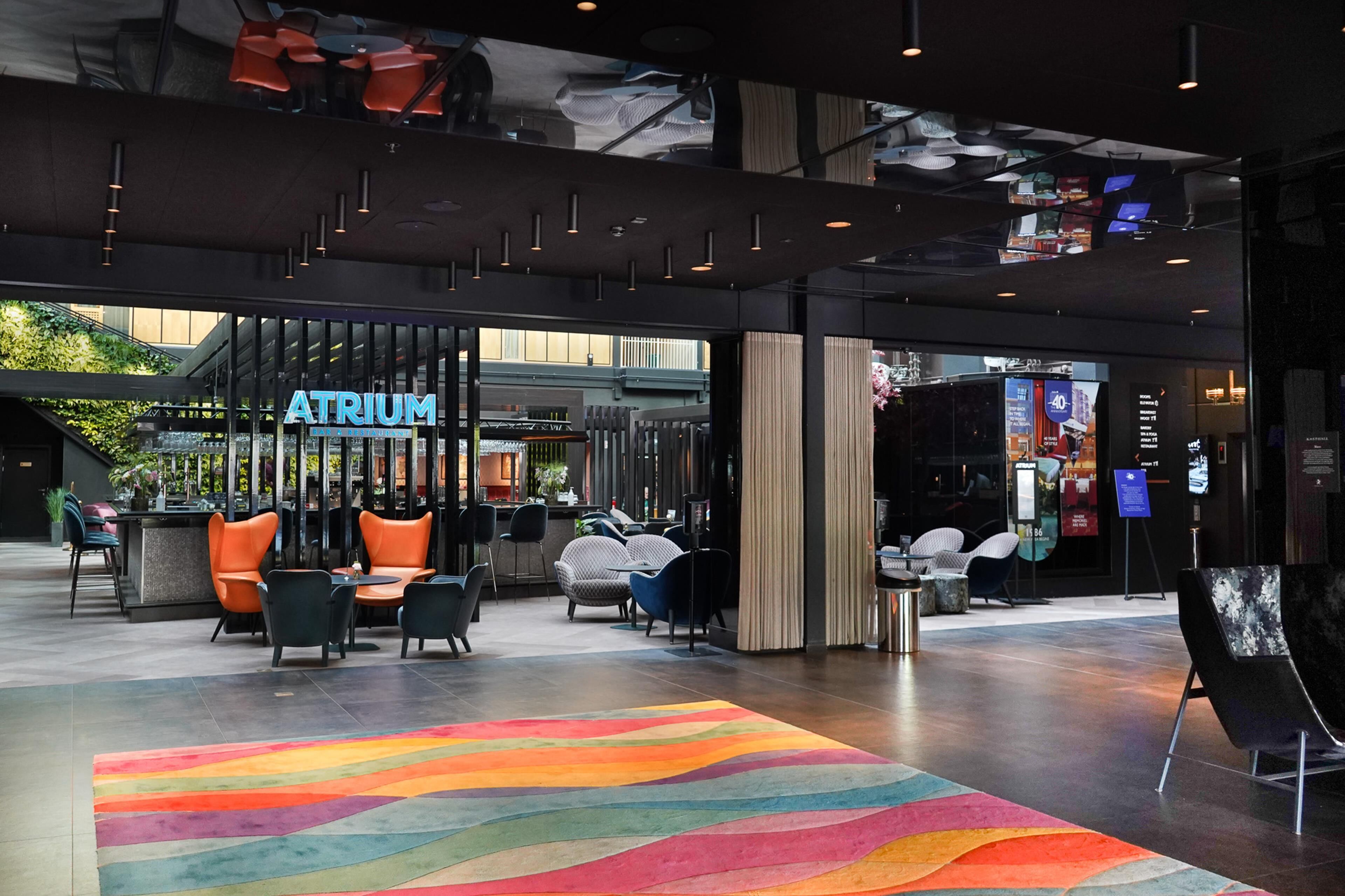 A modern atrium with seating areas, a visible restaurant named 'Atrium,' and a colorful carpet.