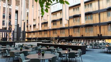 Un amplio espacio exterior con zona de comedor, varias mesas y sillas, rodeado de edificios altos con balcones.