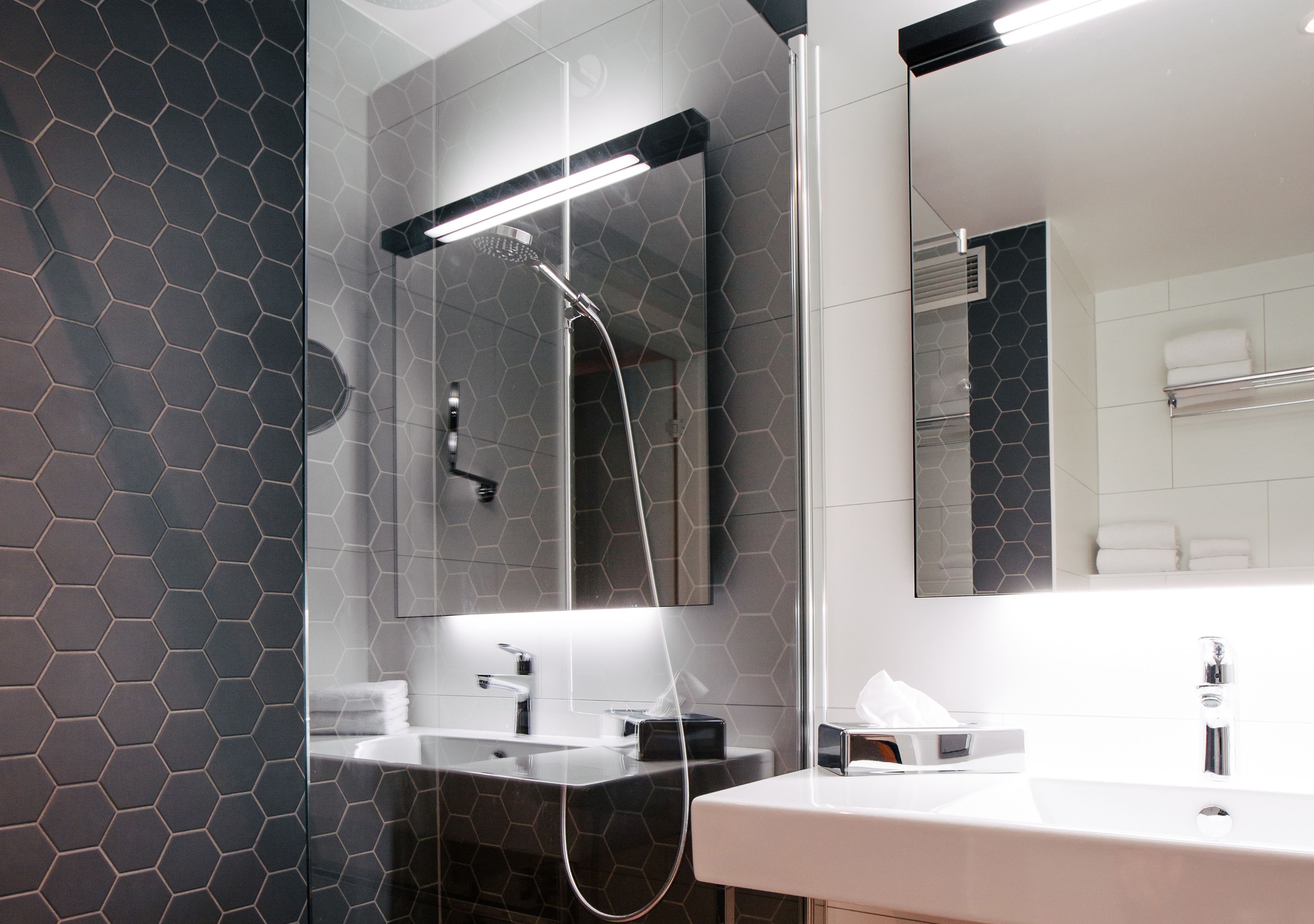 A modern bathroom with a glass shower enclosure, a large mirror, and a white sink.