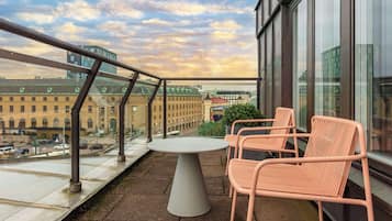 Un balcón con una mesa redonda y dos sillas, con vista a un paisaje urbano con edificios históricos y un cielo despejado.
