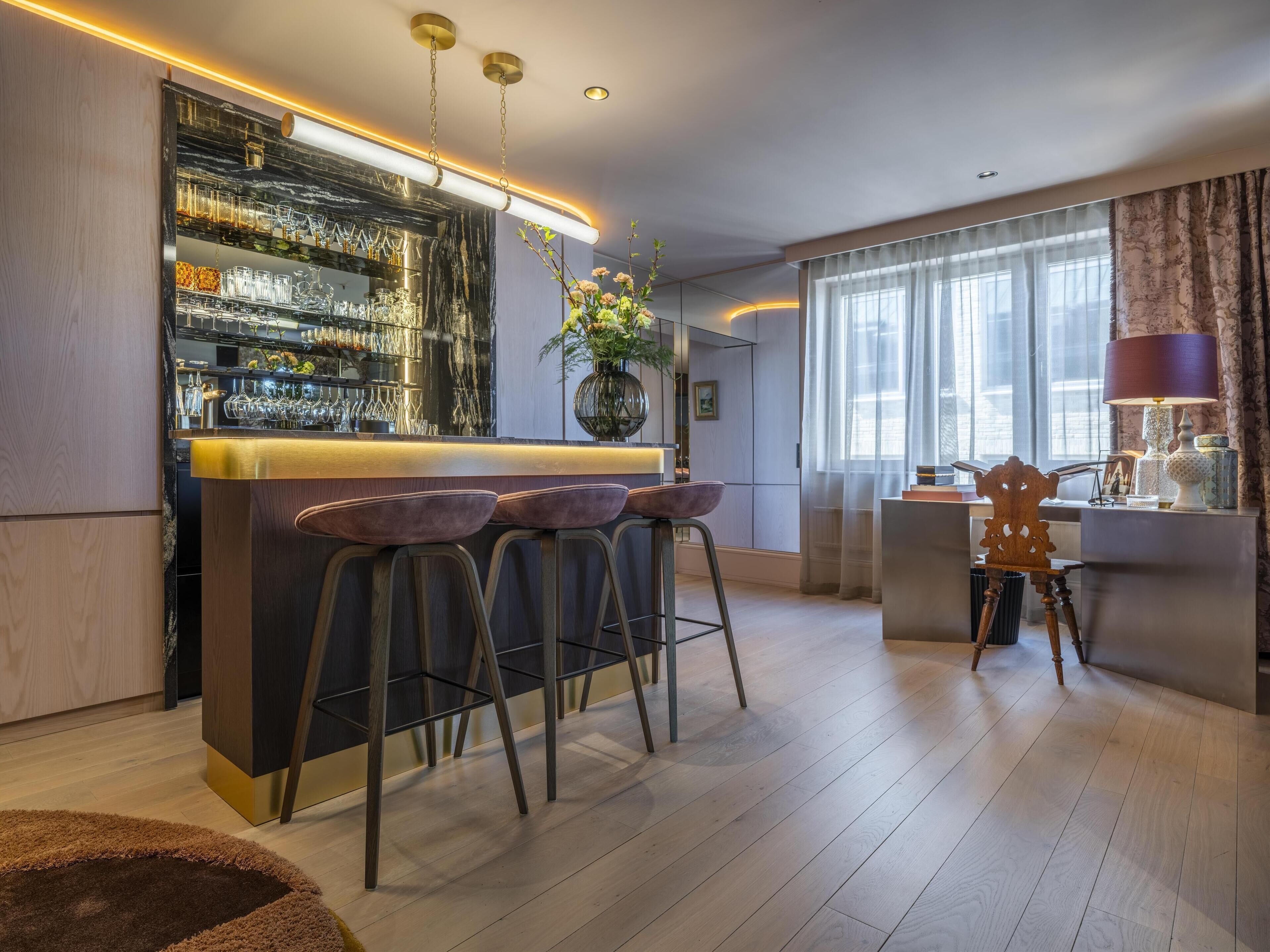 Una cocina moderna con barra, taburetes de madera y un amplio ventanal con cortinas.