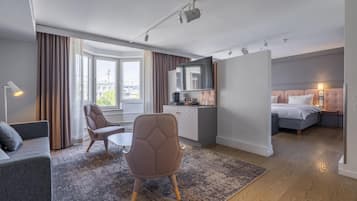 Ett modernt hotellrum med en soffa, en fåtölj, ett litet bord, en säng, ett litet kök och utsikt över staden.