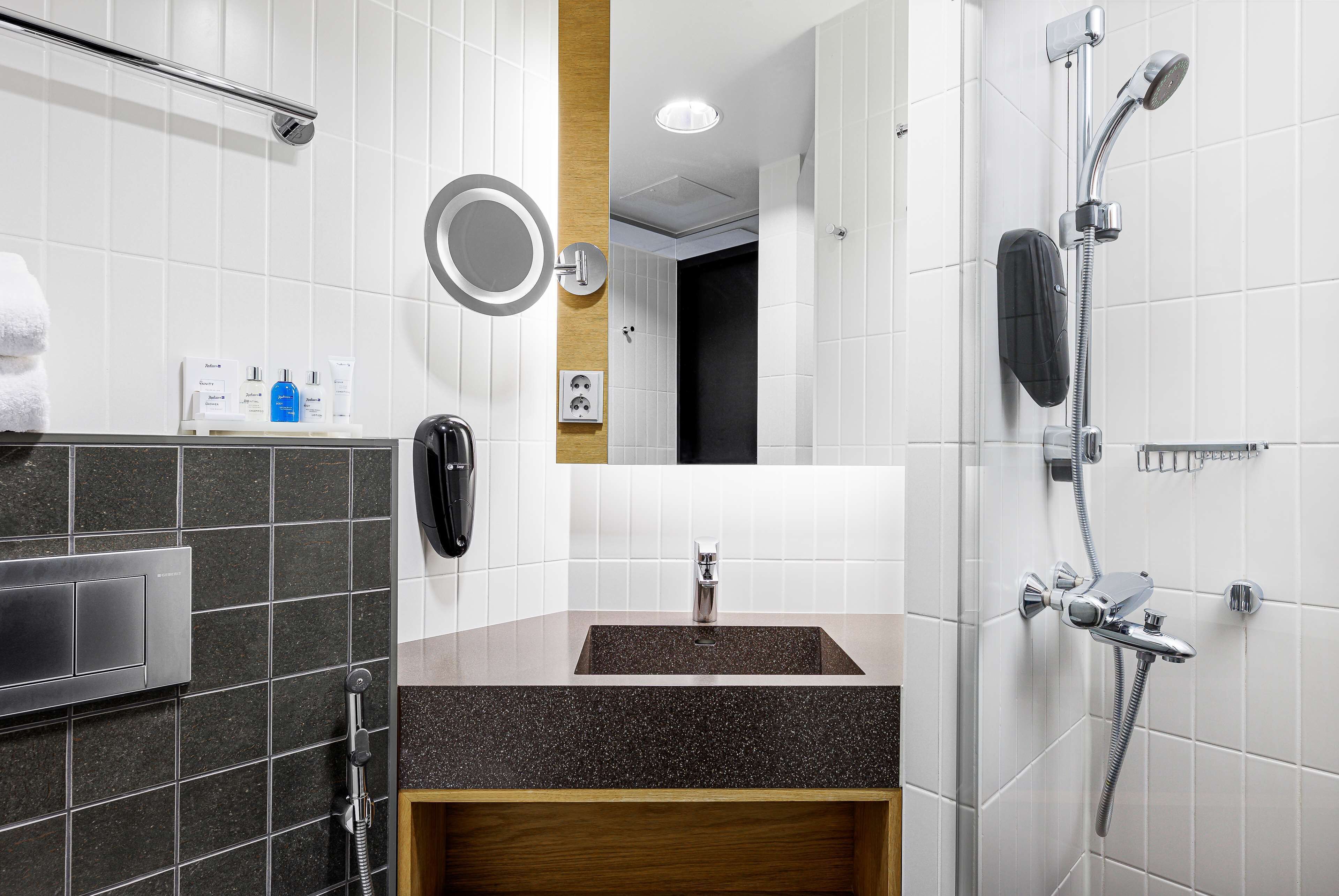 A modern bathroom with a granite countertop sink, a mirror, a handheld showerhead, and a towel rack.