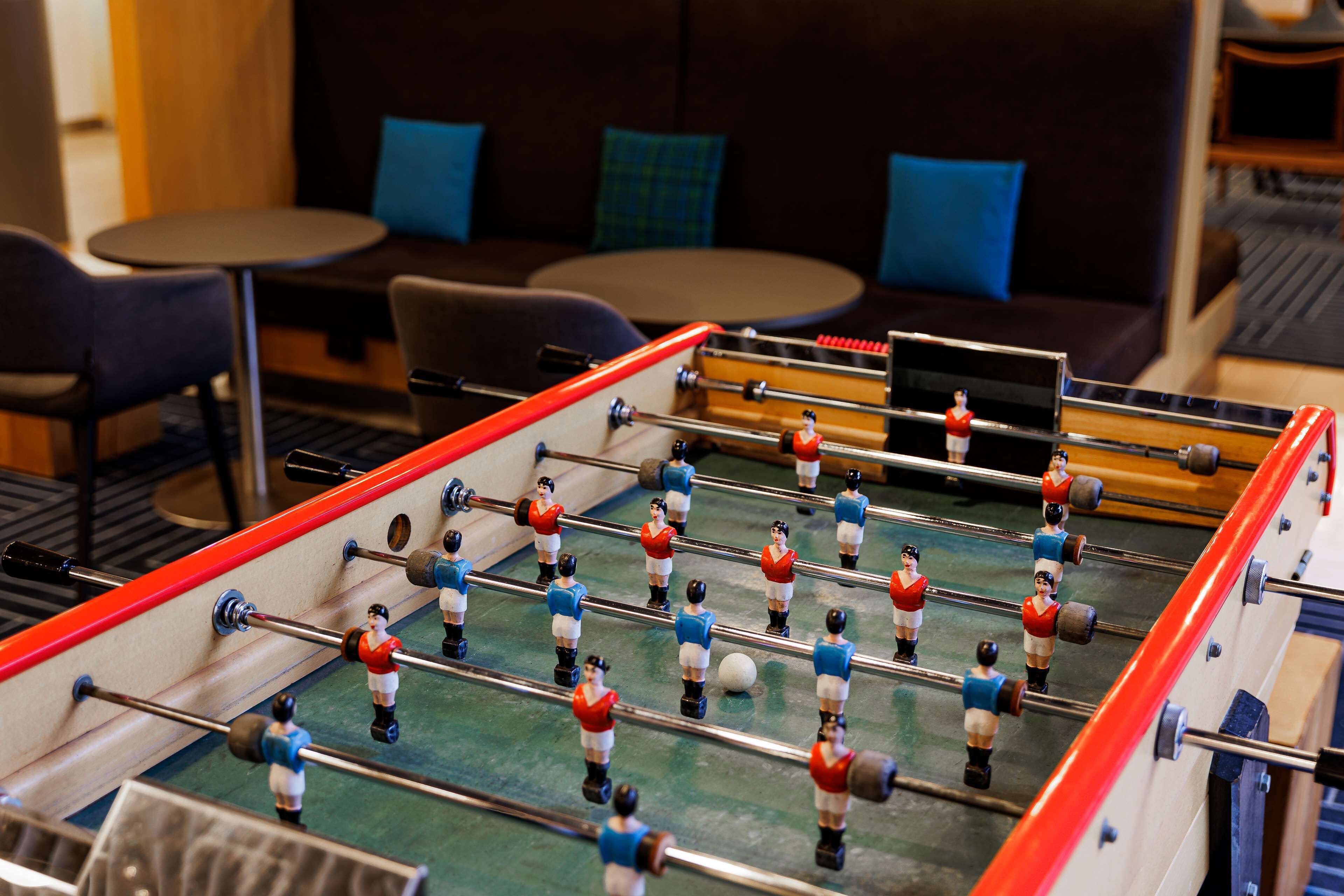 Una mesa de futbolín en una habitación con un sofá y dos mesas redondas pequeñas.