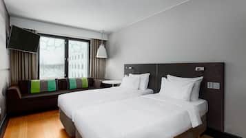 A hotel room with two beds, a sofa, a TV, and a window with curtains.