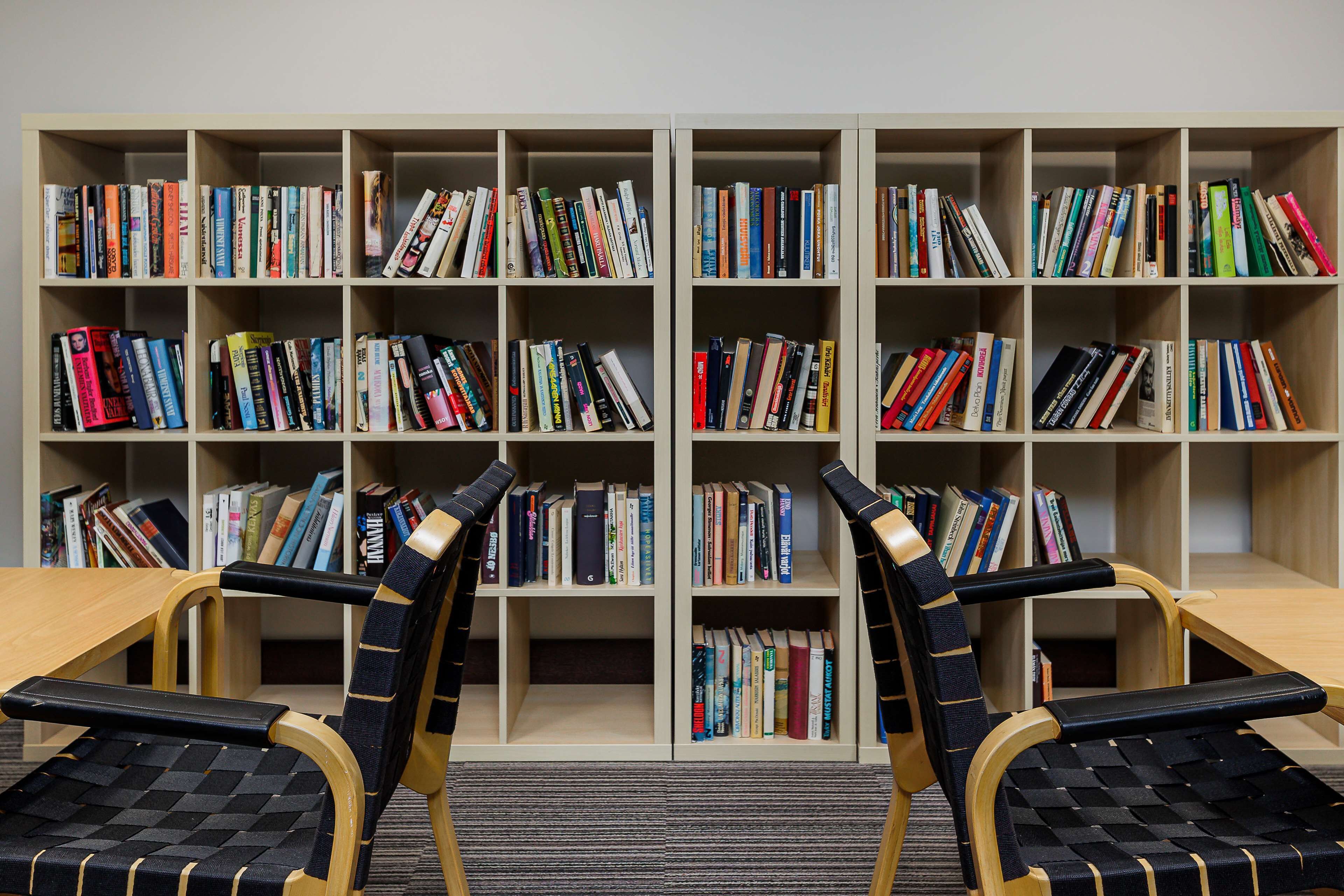 A library with multiple bookshelves filled with books, two wooden chairs with black seats, and a wooden table.