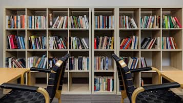 A library with multiple bookshelves filled with books, two wooden chairs with black seats, and a wooden table.