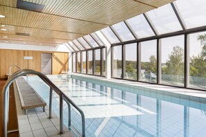 Una piscina con techo de madera y grandes ventanales que dan a las árboles.
