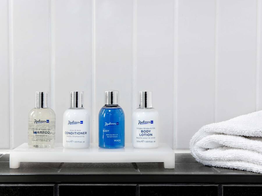 Un estante de baño con cuatro productos de cuidado corporal Radisson: champú, acondicionador, gel de ducha y loción corporal.