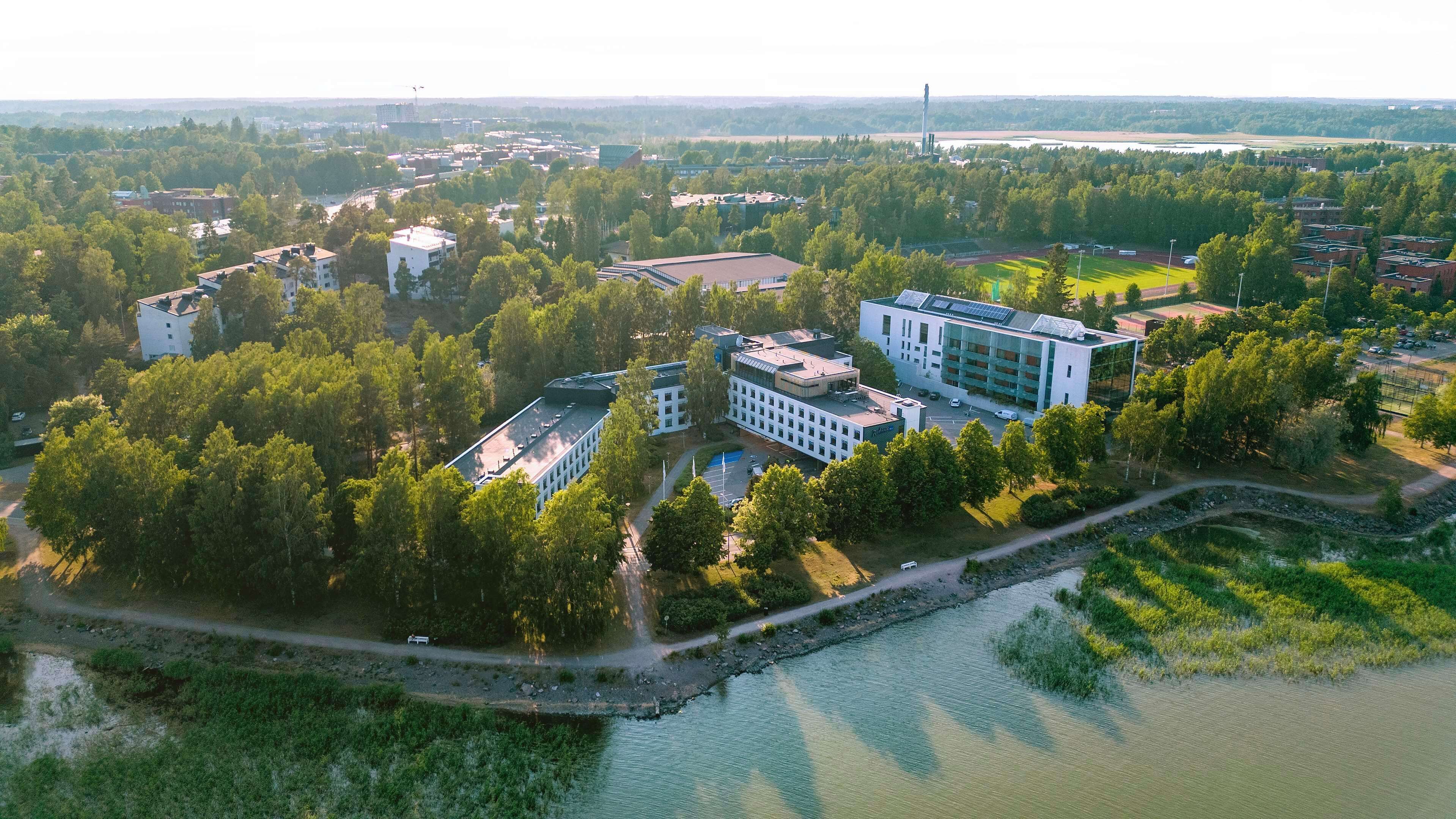 Vista aérea de un campus con varios edificios, un río y zonas verdes circundantes.