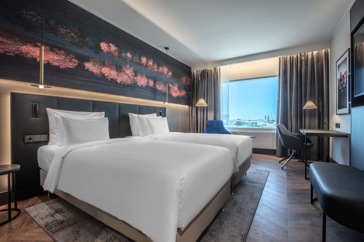 Ein Hotelzimmer mit einem großen Bett, einem Schreibtisch, einem Sessel und Blick auf die Stadt.