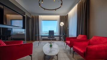 Ein modernes Hotelzimmer mit einem Glastisch, roten Sofas, einem мраморном журнальном столе и einem großen Fenster mit Blick auf die Stadt.
