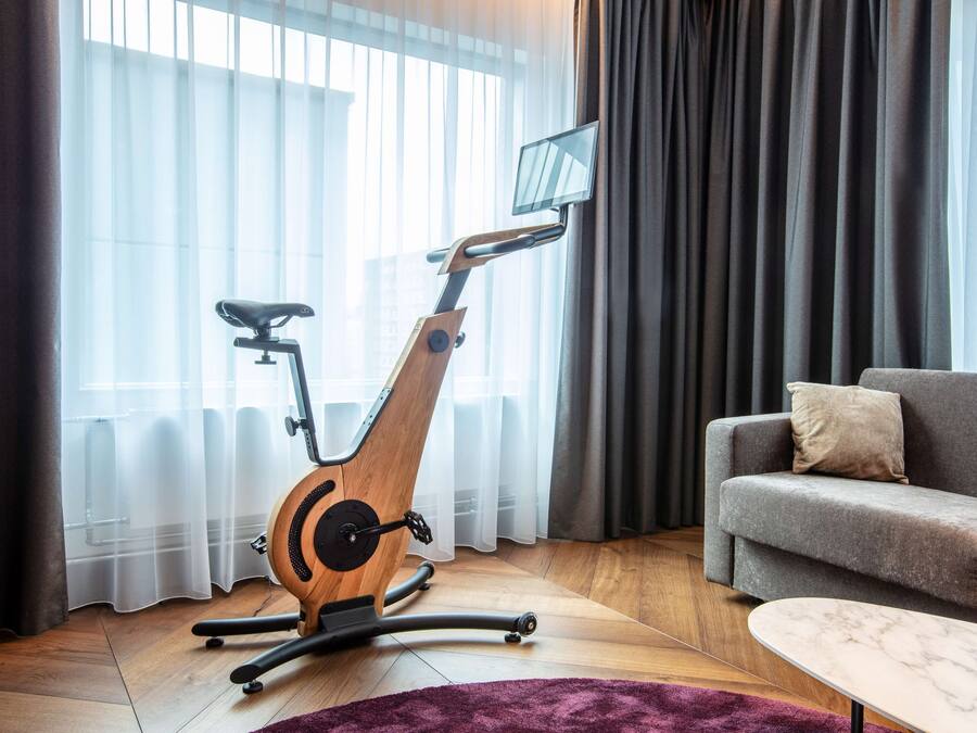 Een moderne woonkamer met een hometrainer, een grijze bank en een marmeren salontafel.