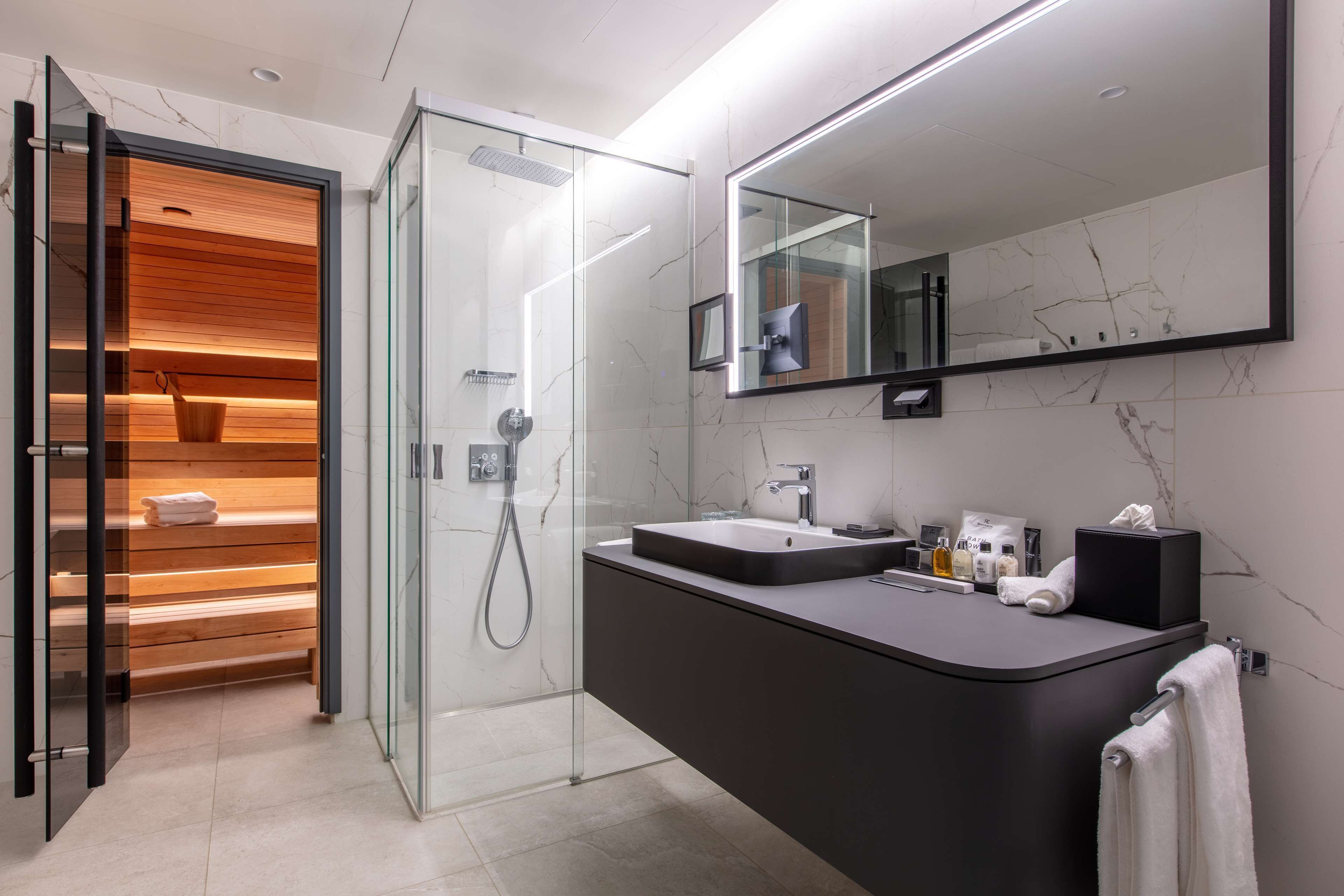 Un baño moderno con cabina de ducha de vidrio, tocador con un espejo grande y un perchero para toallas.