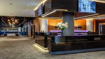 A modern hotel lobby with a reception desk, seating area, and a large screen displaying a welcome message.
