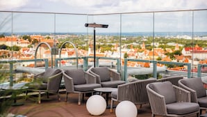 A rooftop terrace with wicker furniture, round tables, and a view of a cityscape. - Radisson Collection Hotel, Tallinn (Tallinn)