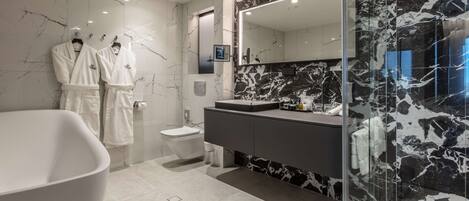 A modern bathroom with a freestanding bathtub, a vanity with a large mirror, and marble walls.