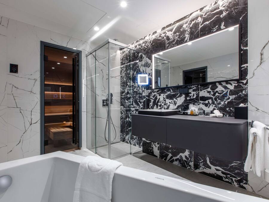 Un bany modern amb paret de marbre, una cabina de dutxa de vidre, un mirall gran i una banyera.