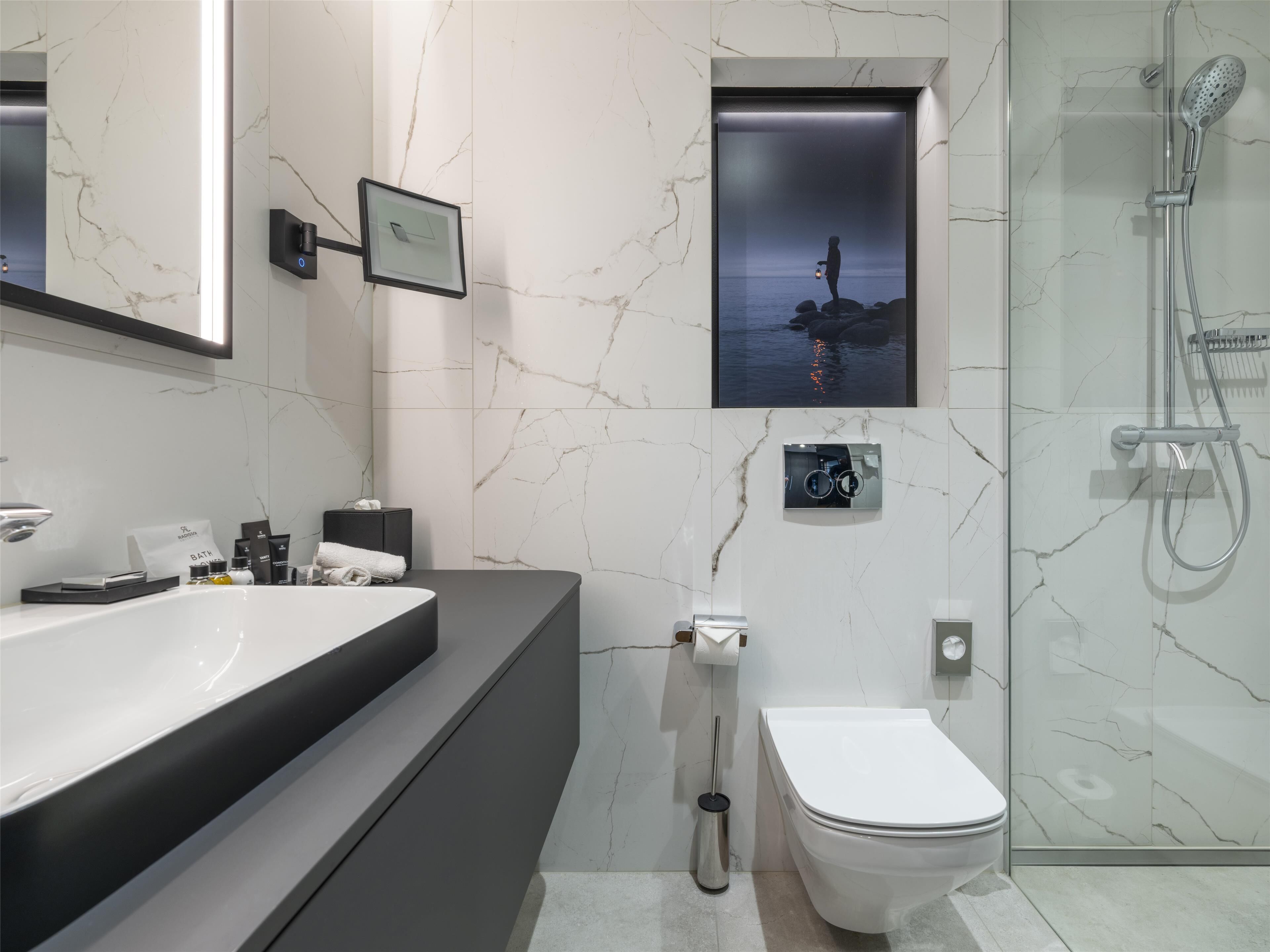 Un baño moderno con un espejo grande, un lavamanos, un inodoro y una ducha.