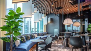 A modern lounge area with a blue sofa, round tables, and chairs, featuring a large plant and large windows. - Radisson Collection Hotel, Tallinn (Tallinn)