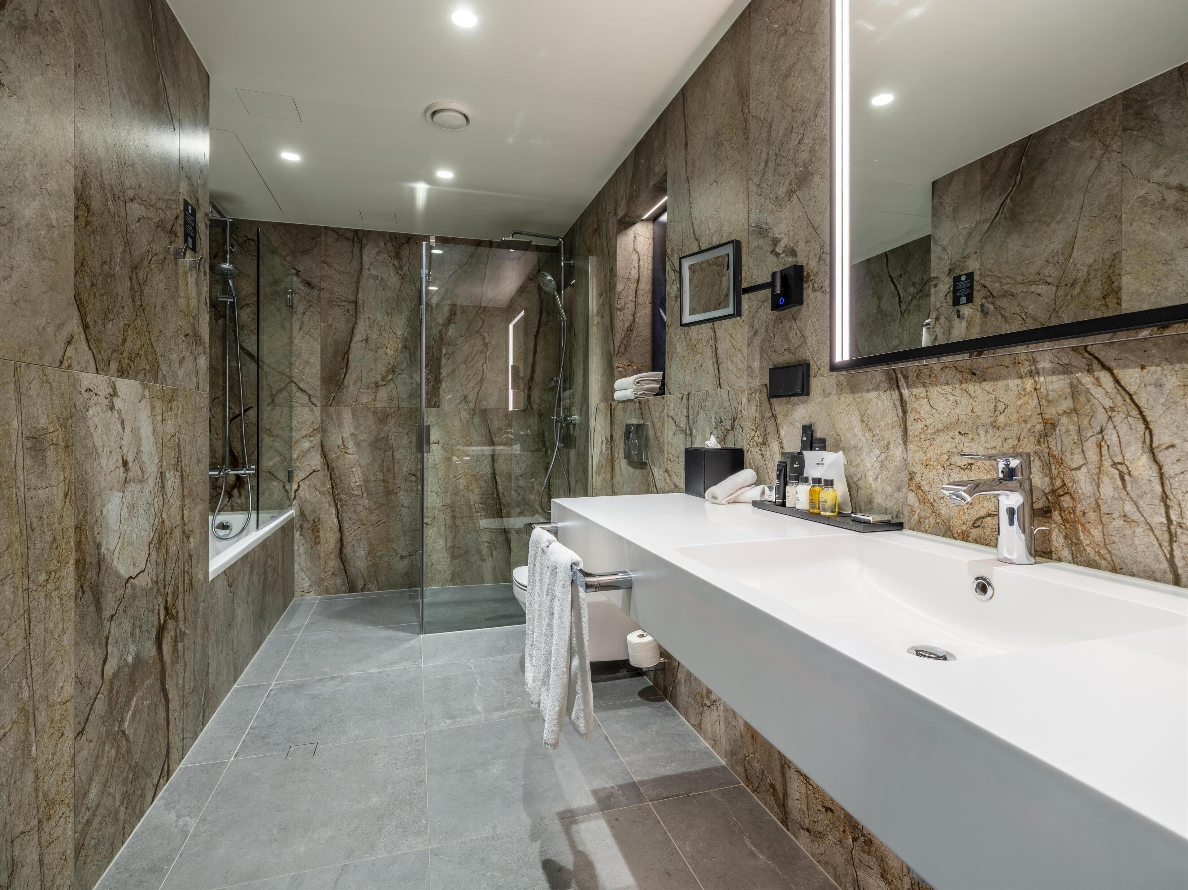 Une salle de bain moderne avec un grand lavabo blanc, une douche en verre et des murs en marbre.
