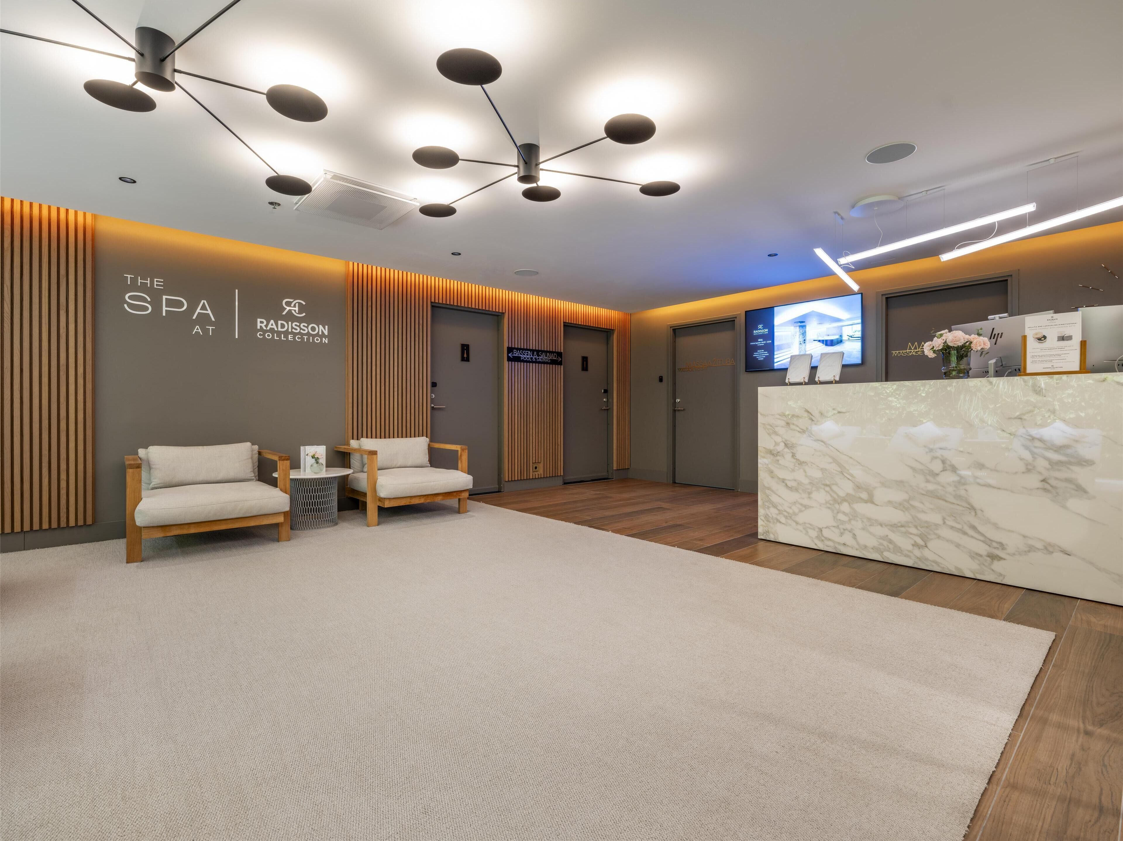 A modern spa reception area with a marble counter, two cushioned chairs, and a ceiling with multiple light fixtures.
