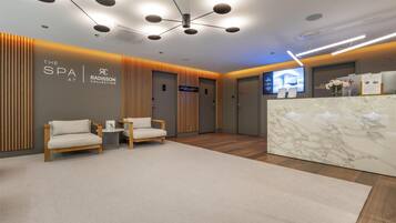 A modern spa reception area with a marble counter, two cushioned chairs, and a ceiling with multiple light fixtures.