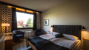 A hotel room with a large bed, a desk, a chair, a window with curtains, and a picture on the wall. - Q Hotel Växjö (Vaxjo)