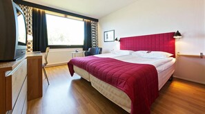 Una habitación de hotel con una cama grande, un escritorio, una silla y un ventanal con cortinas.