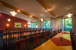 A dining area with multiple tables and chairs, wooden beams on the ceiling, and large windows with patterned curtains. - Q Hotel Växjö (Vaxjo)