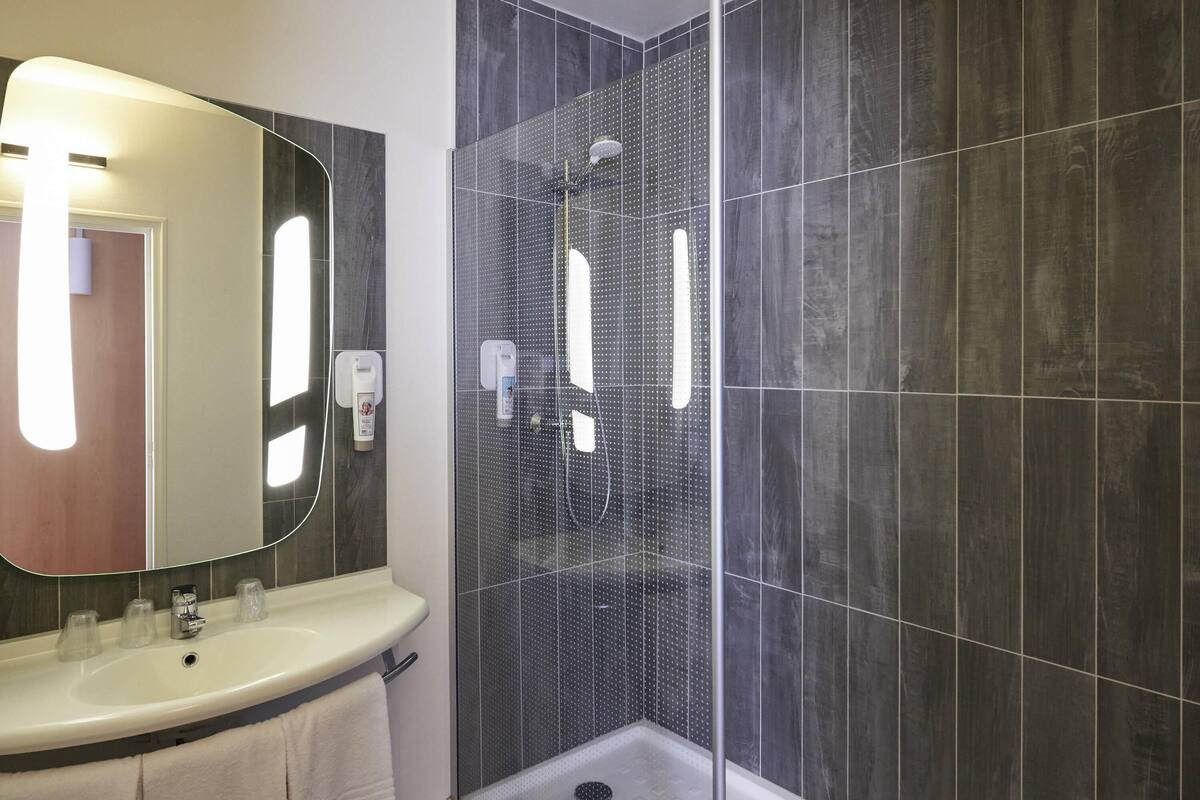 A modern bathroom with a large mirror, a sink, and a shower enclosure.