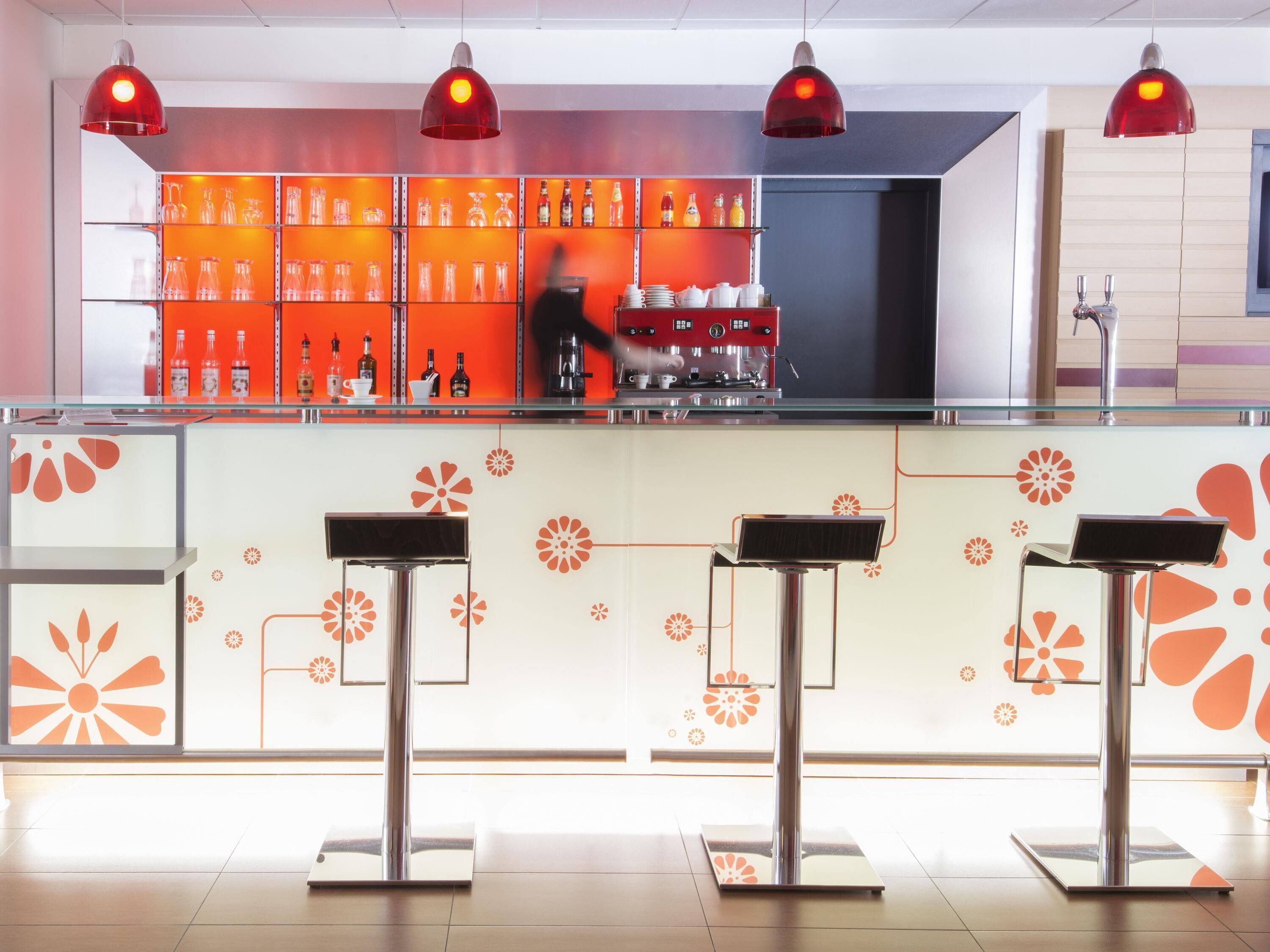 Un espace bar au design moderne, avec un comptoir en verre, des suspensions rouges et un assortiment de bouteilles et de verres.