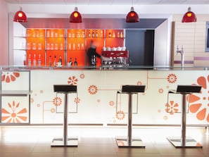 Zona de bar con diseño moderno, que incluye una barra de vidrio, lámparas colgantes rojas y una variedad de botellas y vasos.
