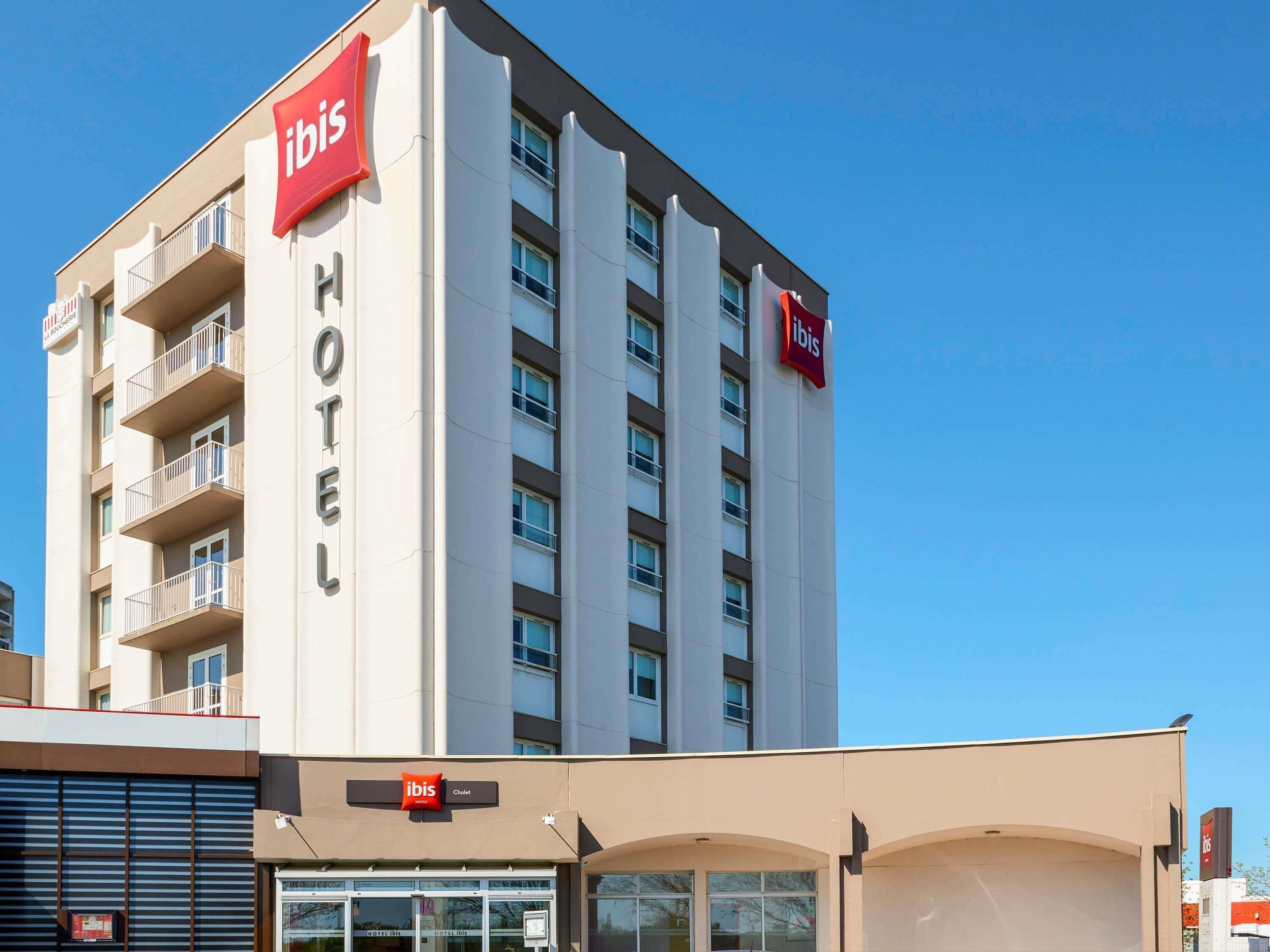 Edifício de hotel com a sinalização 'ibis', entrada visível e uma varanda do lado esquerdo.
