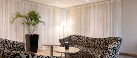 Una sala de estar moderna con sofás estampados, una mesita redonda pequeña, una planta en maceta y una lámpara.