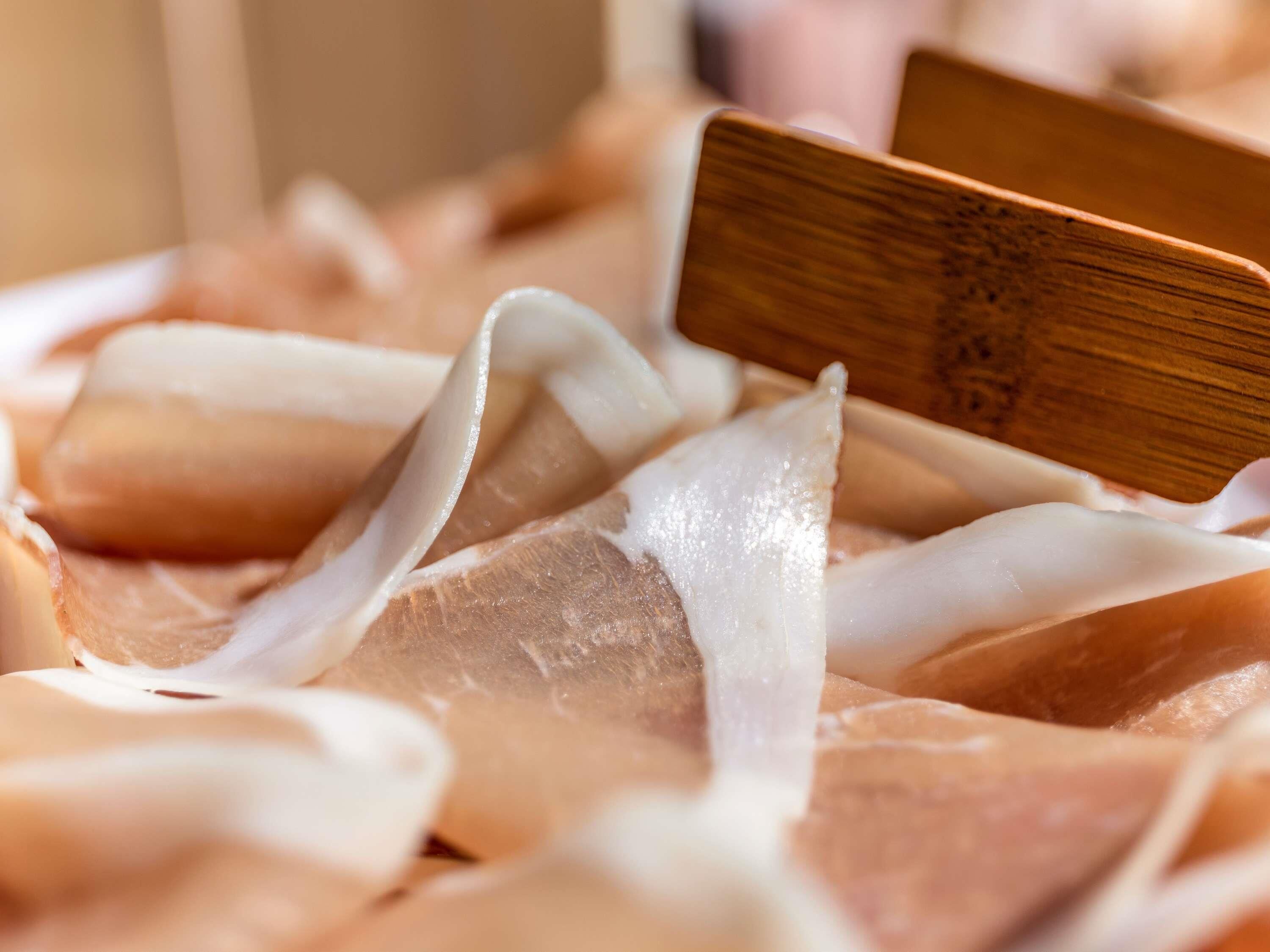 A close-up of a wooden cutting board with a white, translucent material, possibly cheese or a similar food item, on it.