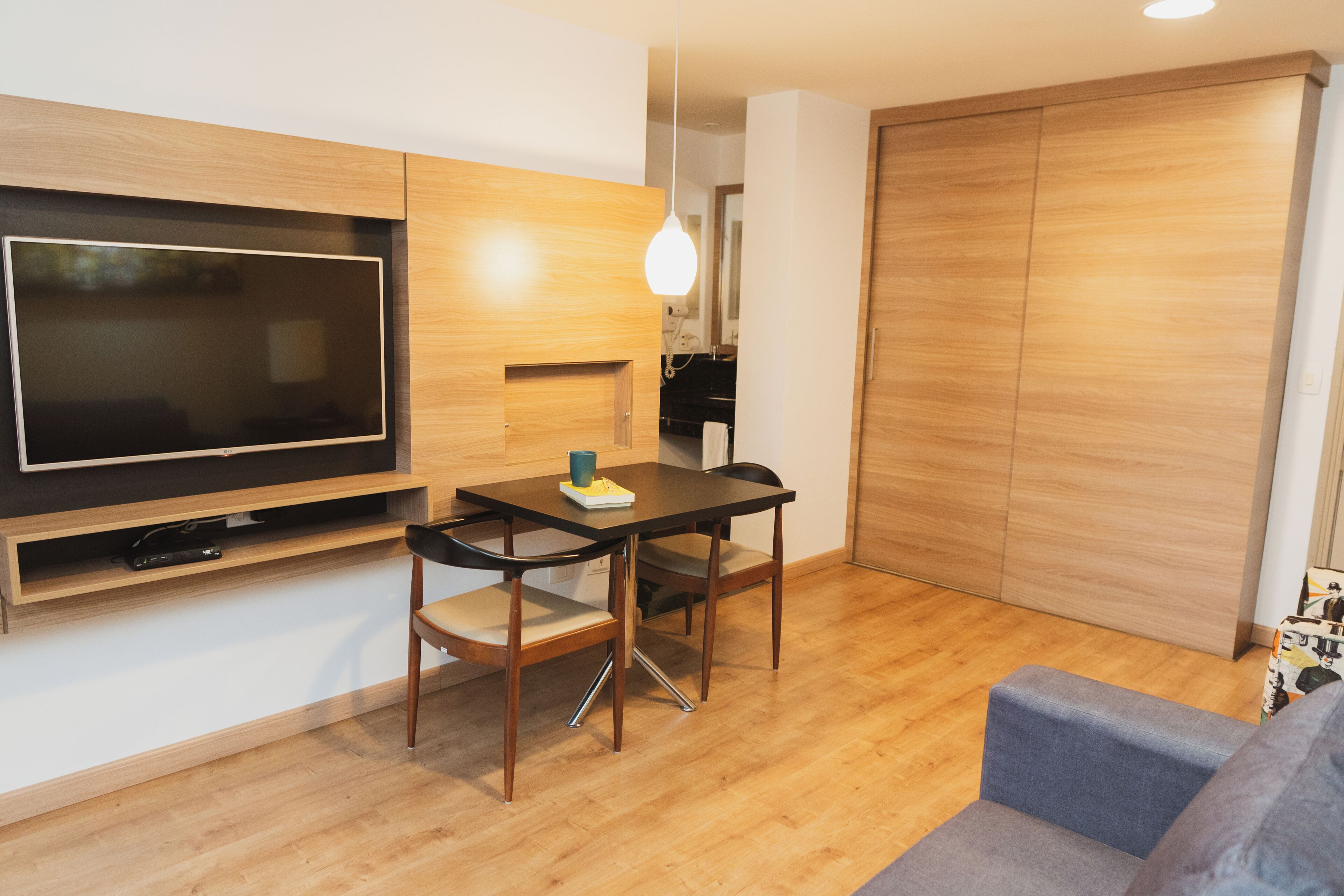 A modern living room with a flat-screen TV, wooden flooring, a dining table with chairs, a sofa, and a wardrobe.